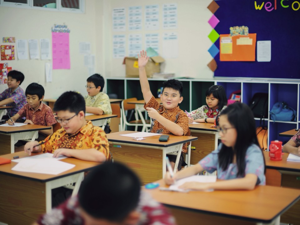 一間教室裡孩子們在座位上作業，其中一人舉手