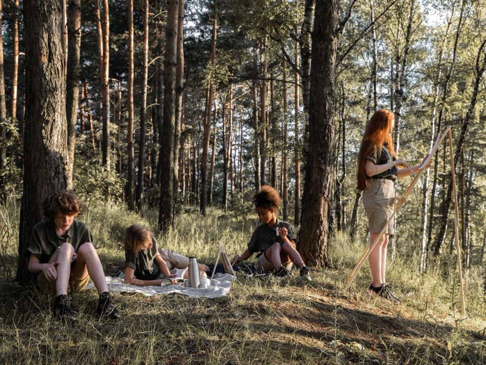 Children reading and sketching on a blanket in a forest