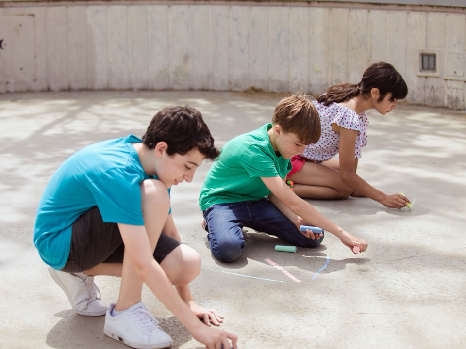 Three children drawing with chalk on the ground outdoors