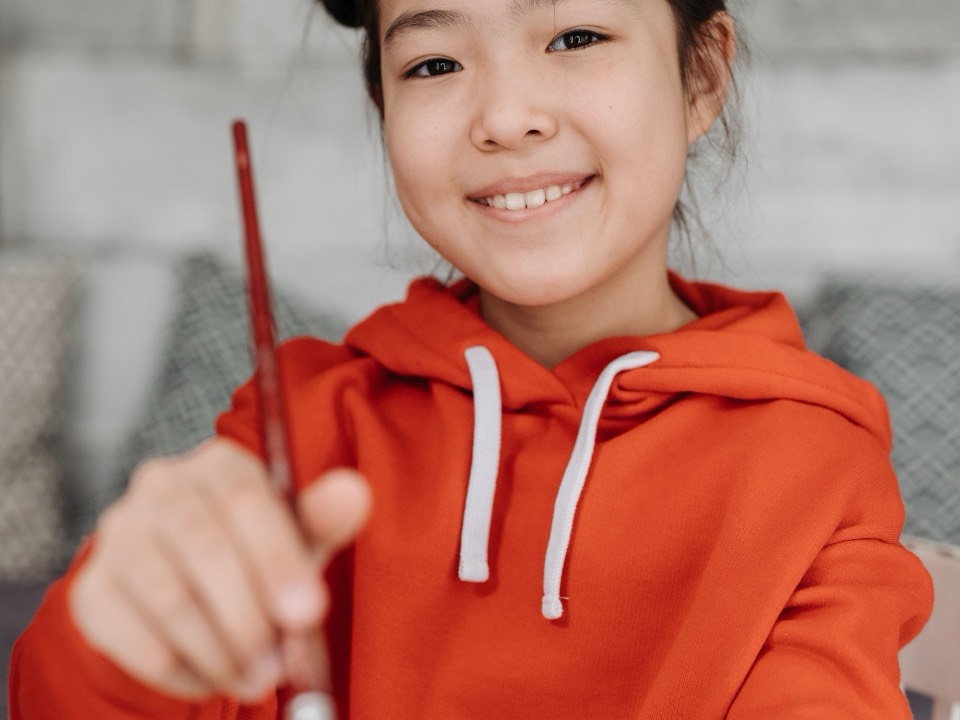A girl holding up a paintbrush and smiling
