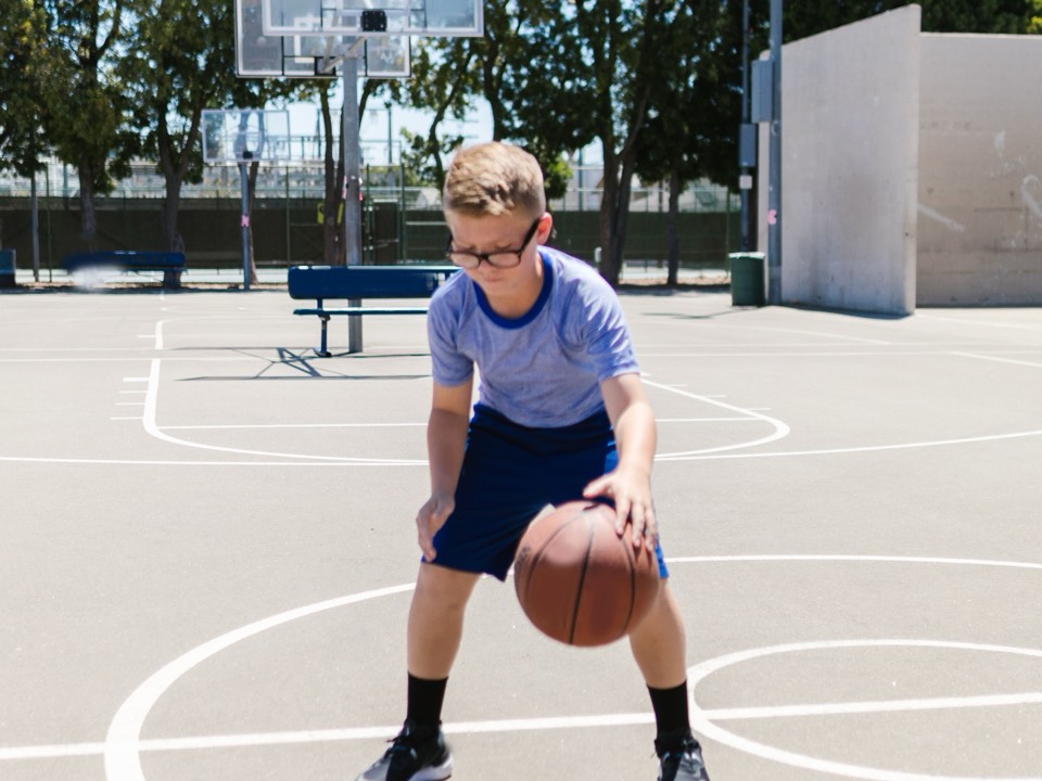 A boy dribbling a basketball on an outdoor court